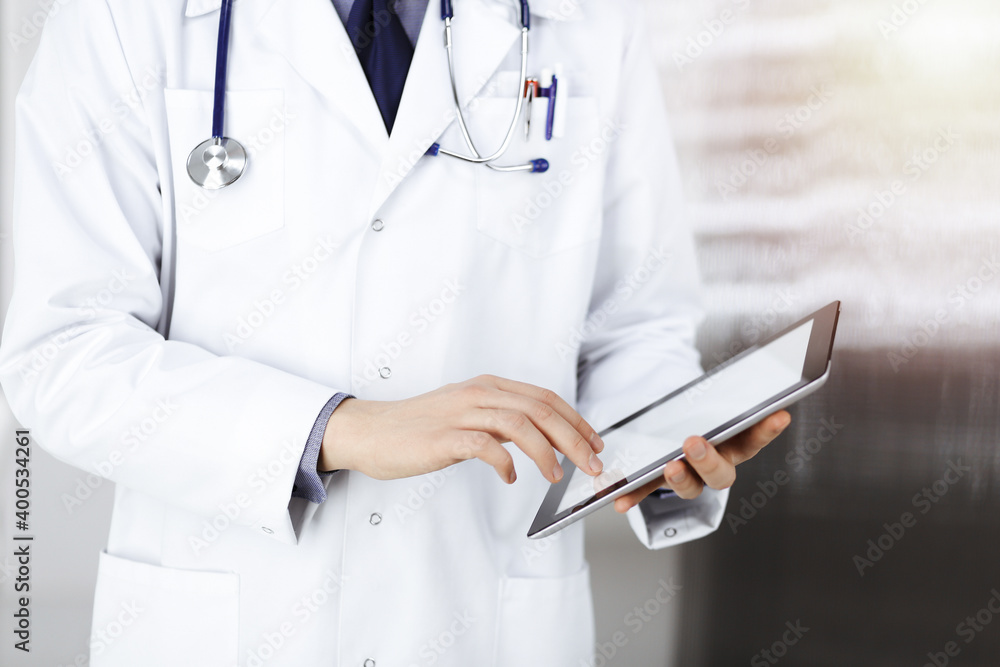 Unknown male doctor using tablet computer in sunny clinic, closeup. Perfect medical service in hospital. Medicine and healthcare concept Unknown male doctor using tablet computer in sunny clinic, closeup. Perfect medical service in hospital. Medicine and healthcare concept