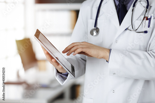 Unknown male doctor using tablet computer in sunny clinic, closeup. Perfect medical service in hospital. Medicine and healthcare concept