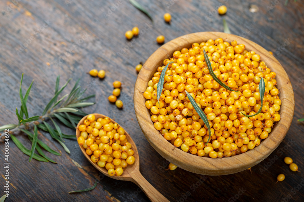 Sea buckthorn with leaves in a wooden bowl on a wooden table. Sea buckthorn with leaves in a wooden bowl on a wooden table.