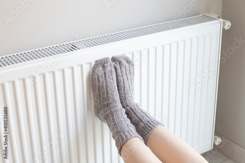Woman is warm knitted woolen socks near a home heater in cold winter time. Using heater at home in winter.