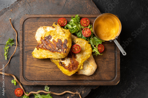 Juicy chicken breast fried on a barbecue until golden brown with homemade sauce, cherry tomatoes and lettuce. Grilled chicken. A hot poultry main course. photo