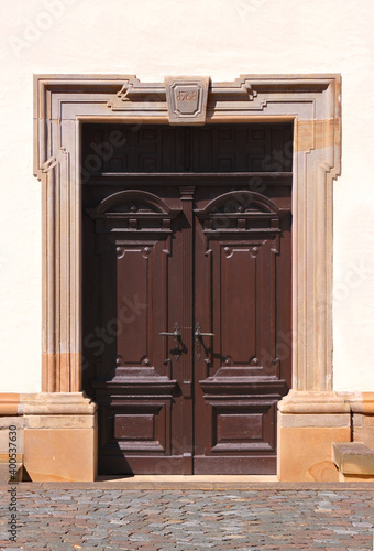 Brown wooden door in a baroque sandstone portal with an old keystone on the facade of the Rehborn village church in Germany