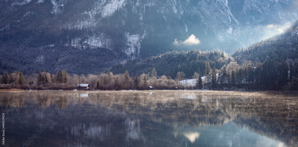 una casita a la orilla de un lago con montañas de fondo nevadas 