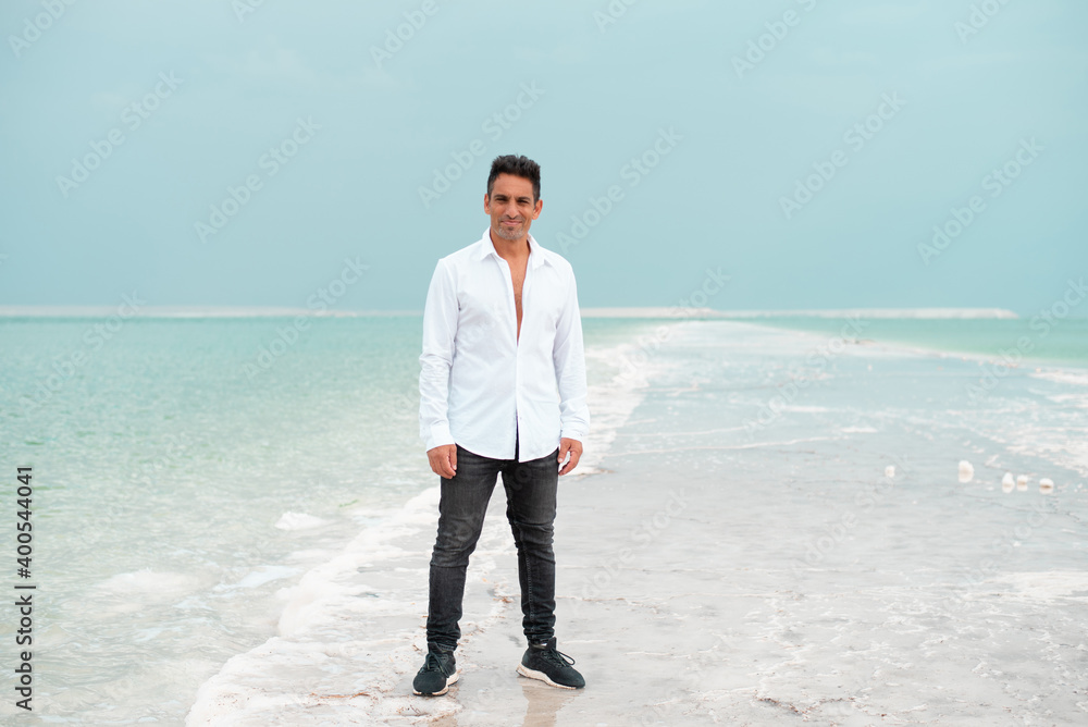 Young businessman stand on the white beach of dead sea. Blue sea paradise for summer holidays. The blue sky merges with endless surfase of the sea. vacation and travel in Israel. Young businessman stand on the white beach of dead sea. Blue sea paradise for summer holidays. The blue sky merges with endless surfase of the sea. vacation and travel in Israel.