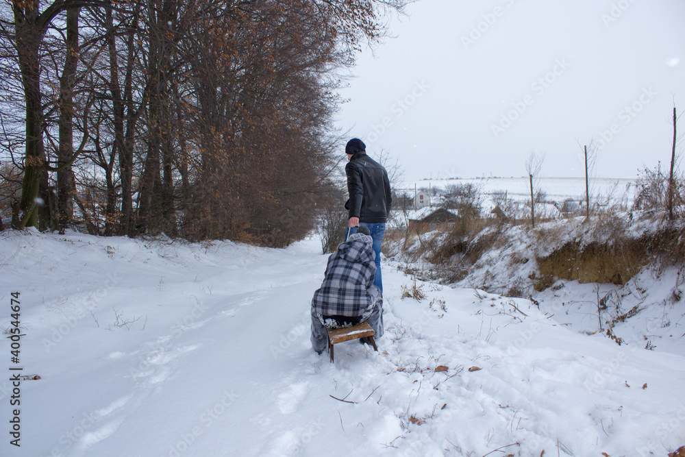 man pulls a sled with a boy,older brother pulls a little boy in the winter on a sled