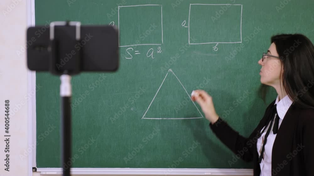 Online schooling, e-learning. Female teacher is holding online lesson, remotely, using smartphone webcam. live stream for students, from school class. remote teaching, learning during coronavirus Online schooling, e-learning. Female teacher is holding online lesson, remotely, using smartphone webcam. live stream for students, from school class. remote teaching, learning during coronavirus