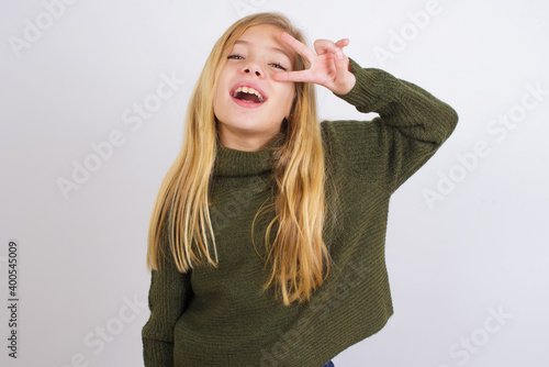 Wallpaper Mural Caucasian kid girl wearing green knitted sweater against white wall Doing peace symbol with fingers over face, smiling cheerful showing victory Torontodigital.ca
