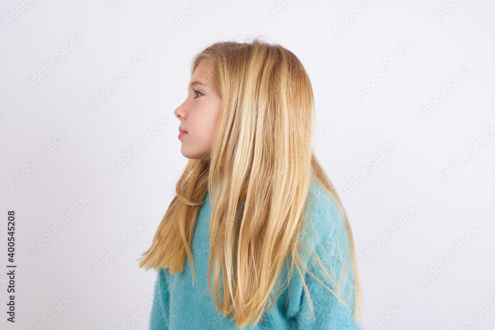 Side view of young happy smiling Cute Caucasian kid girl wearing blue knitted sweater against white wall Side view of young happy smiling Cute Caucasian kid girl wearing blue knitted sweater against white wall