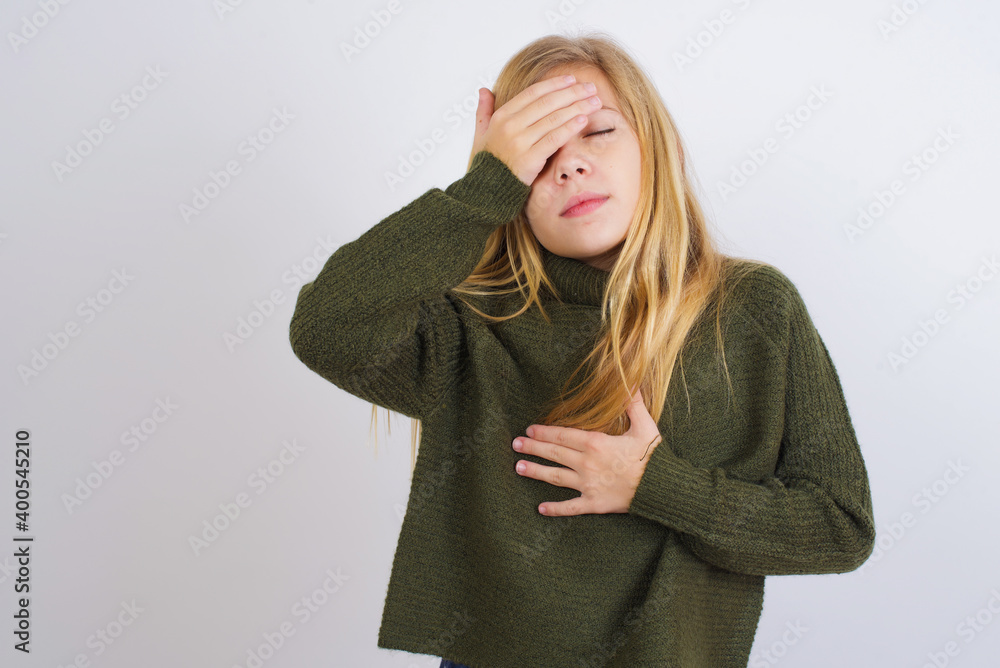 Fototapeta premium Caucasian kid girl wearing green knitted sweater against white wall Touching forehead for illness and fever, flu and cold, virus sick.