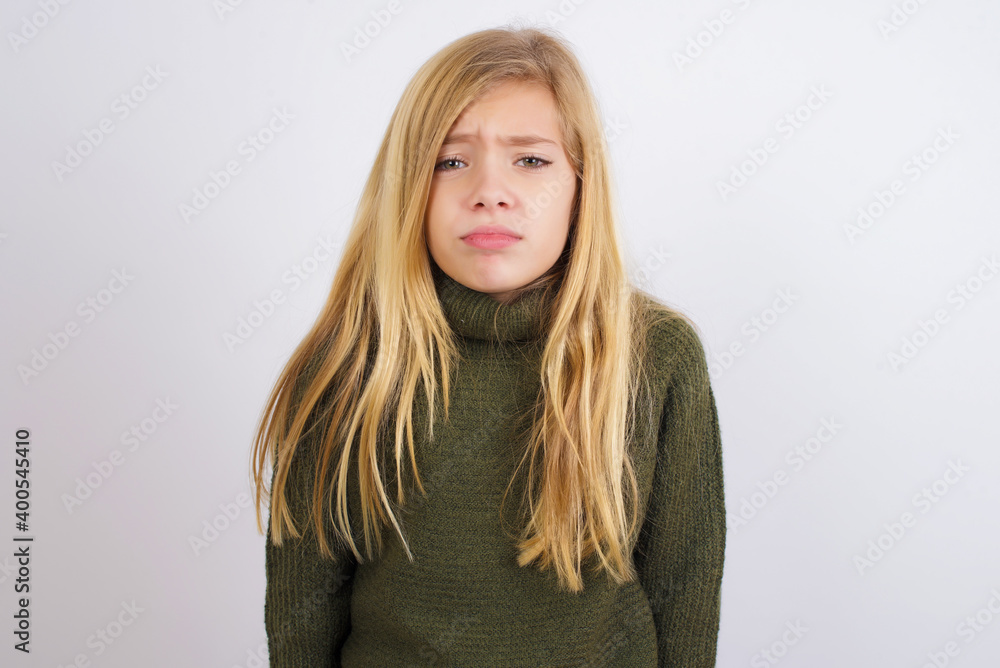 Displeased upset Caucasian kid girl wearing green knitted sweater against white wall frowns face as going to cry, being discontent and unhappy as can't achieve goals, Disappointed model has troubles Displeased upset Caucasian kid girl wearing green knitted sweater against white wall frowns face as going to cry, being discontent and unhappy as can't achieve goals, Disappointed model has troubles