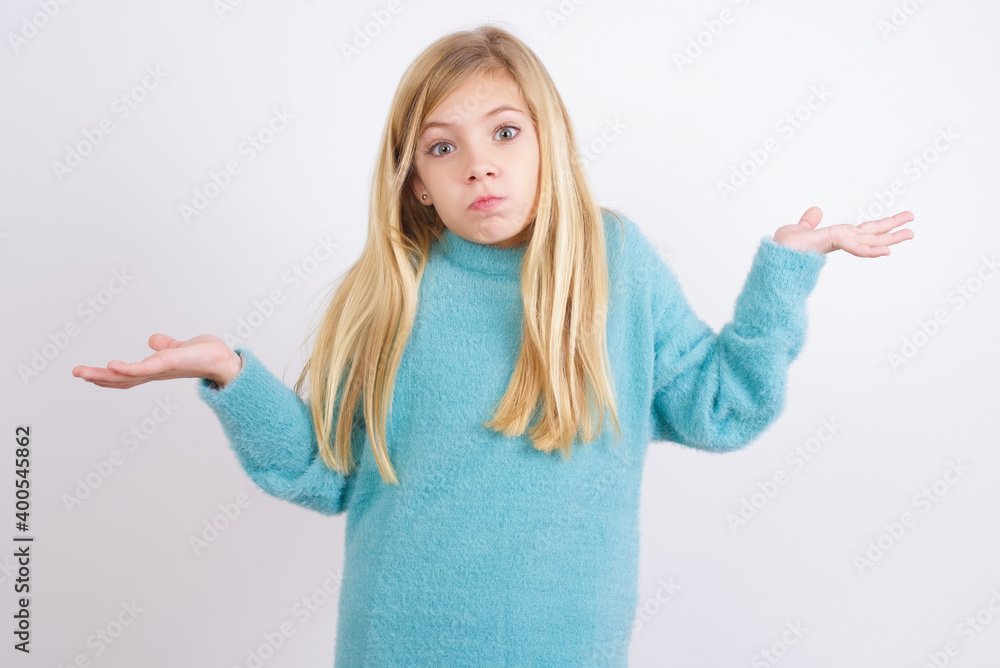 Puzzled and clueless Cute Caucasian kid girl wearing blue knitted sweater against white wall with arms out, shrugging shoulders, saying: who cares, so what, I don't know. Puzzled and clueless Cute Caucasian kid girl wearing blue knitted sweater against white wall with arms out, shrugging shoulders, saying: who cares, so what, I don't know.