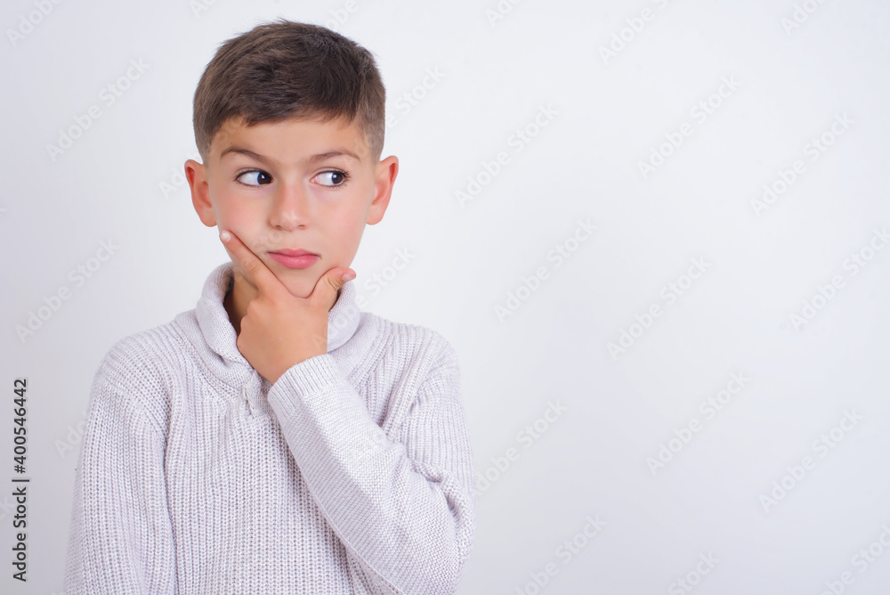 Cute Caucasian kid boy wearing knitted sweater against white wall Thinking worried about a question, concerned and nervous with hand on chin. Cute Caucasian kid boy wearing knitted sweater against white wall Thinking worried about a question, concerned and nervous with hand on chin.