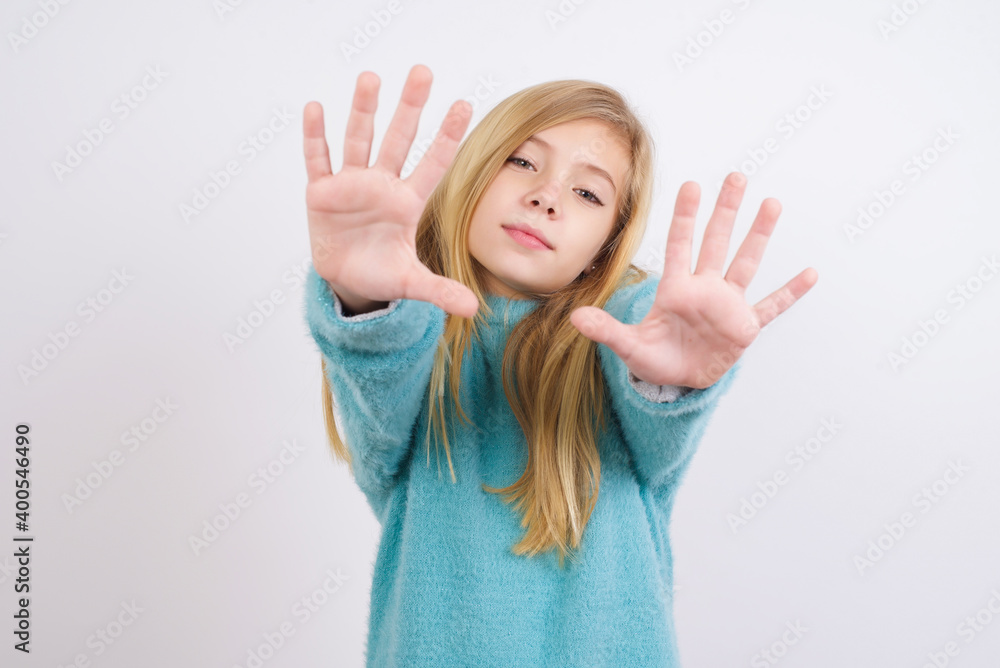 Portrait of smiling Cute Caucasian kid girl wearing blue knitted sweater against white wall looking at camera and gesturing finger frame. Creativity and photography concept. Portrait of smiling Cute Caucasian kid girl wearing blue knitted sweater against white wall looking at camera and gesturing finger frame. Creativity and photography concept.