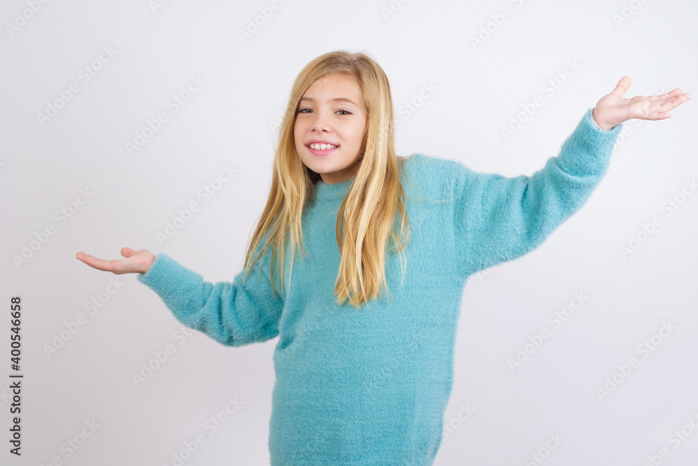 Cheerful Cute Caucasian kid girl wearing blue knitted sweater against white wall making a welcome gesture raising arms over head. Cheerful Cute Caucasian kid girl wearing blue knitted sweater against white wall making a welcome gesture raising arms over head.