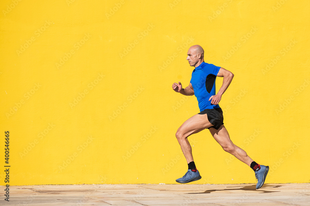 Sportsman running in the street in front of a yellow wall Sportsman running in the street in front of a yellow wall