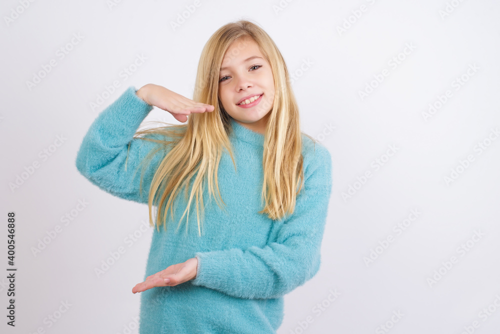 Cute Caucasian kid girl wearing blue knitted sweater against white wall gesturing with hands showing big and large size sign, measure symbol. Cute Caucasian kid girl wearing blue knitted sweater against white wall gesturing with hands showing big and large size sign, measure symbol.