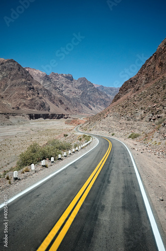Empty asphalt highway road with curves and yellow dividing line in a desert valley in Andes Mountains - Mendoza province - Argentina