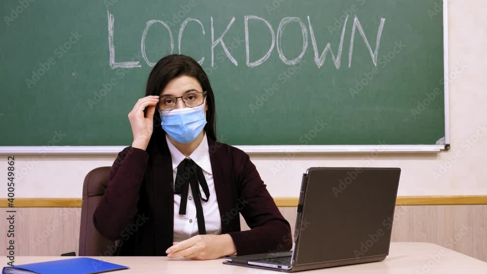 remote teaching, lockdown at schools. Online schooling, e-learning. Female teacher, in protective mask, is holding online lesson for students, remotely from school class, using web cam. Online remote teaching, lockdown at schools. Online schooling, e-learning. Female teacher, in protective mask, is holding online lesson for students, remotely from school class, using web cam. Online