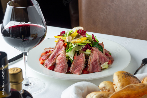 Delicious steak salad with red wine and freshly baked baguette. white table with leather chair in a restaurant