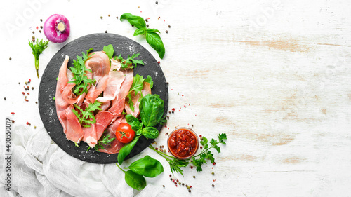 Prosciutto with arugula and basil on a black plate. Spanish cuisine. Top view. Free space for your text.