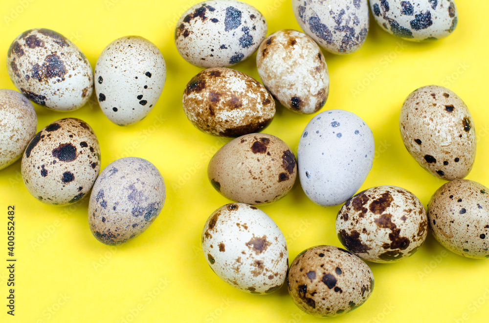 Many quail eggs lie on a yellow background, close-up