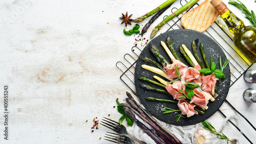 Prosciutto with boiled asparagus and spices on a black stone plate. Top view. Free space for your text.