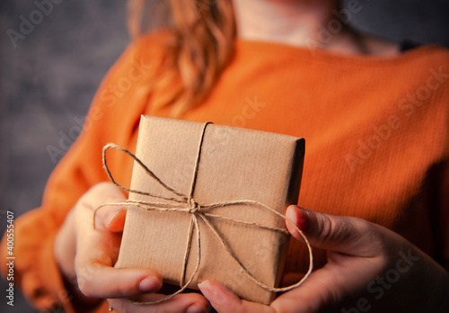 Young Female holding a kraft gift box  wrapped in plain brown paper  Valentines day  Birthday  Mothers Day present or gift concept selective focus  dark background