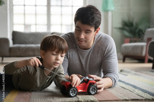 Close up father and little son playing, fixing toy car, lying on warm floor with underfloor heating at home, cute adorable boy using screwdriver, having fun with dad, enjoying leisure time