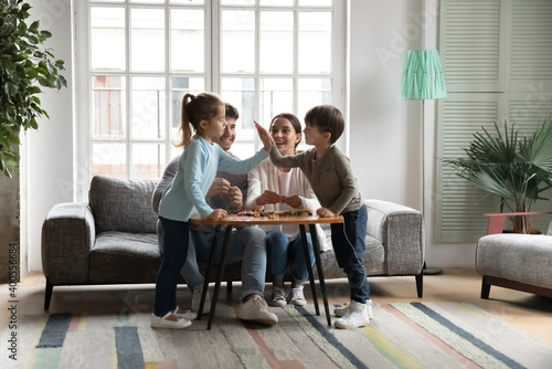 Happy parents with two kids having fun with colorful beads, sitting at table on cozy couch at home, cute adorable little daughter and son giving high five, family enjoying leisure time together