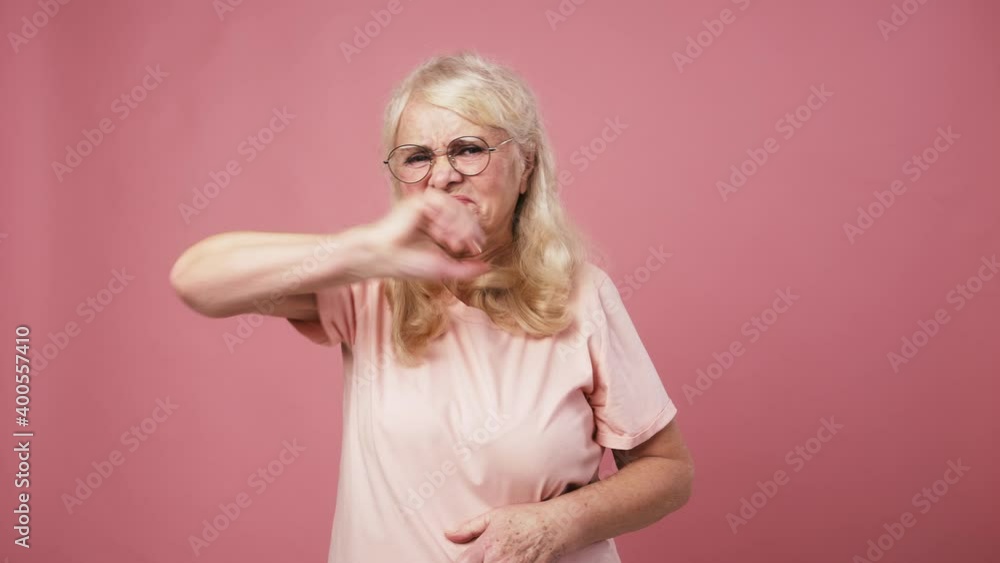 Grumpy senior woman looking at camera and gesturing thumb up gesture, pink studio background Grumpy senior woman looking at camera and gesturing thumb up gesture, pink studio background