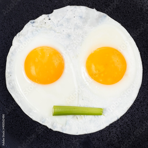 fried eggs and piece of celery on black plate close up. Fried eggs like face with straigh closed mouth photo