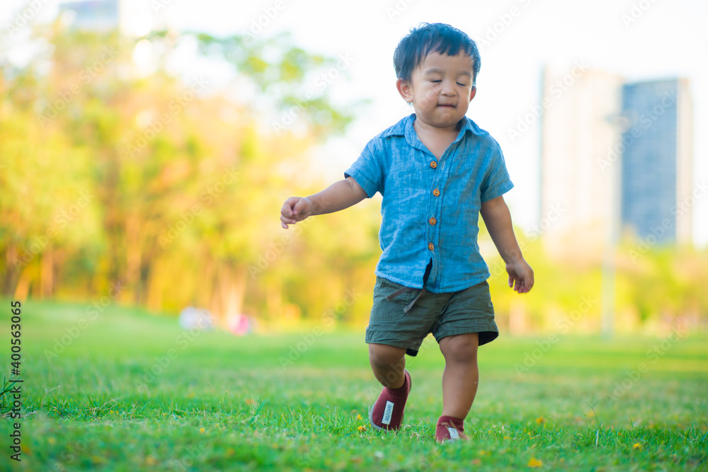 Little boy running on green grass in city park sunset time with tree Little boy running on green grass in city park sunset time with tree