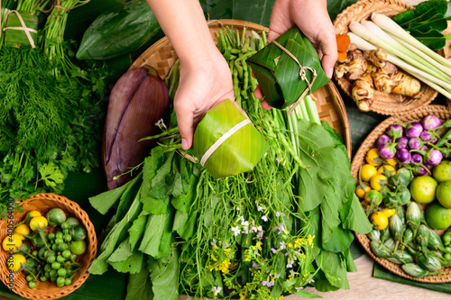 Hand holding food wrapped by banana leaf and fresh organic Asian vegetables from local farmer market, Northern Thailand photo