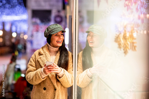 Beautiful young woman with mobile phone by the shop window at Christmas time