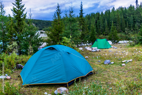 tents in a clearing among fir trees on the river bank