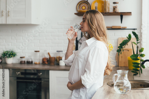 Pregnant girl drinking clean water in the kitchen