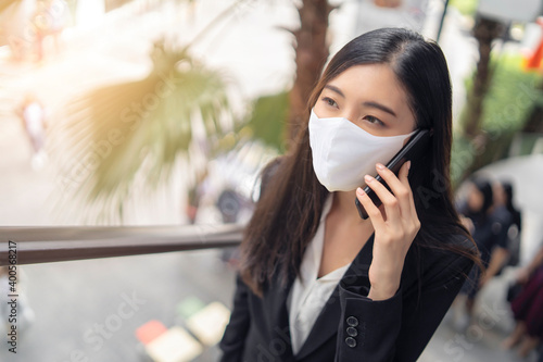 Asian business woman wearing face mask out public city distancing health and safety COVID-19 pandemic contacting with smartphone talking or calling people happy and smiling commuting to work place © Have a nice day 