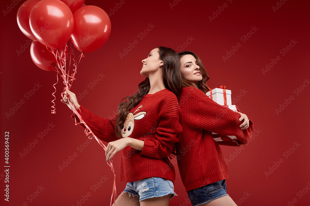 Two pretty twins in winter sweater with party balloons and gift boxes Two pretty twins in winter sweater with party balloons and gift boxes