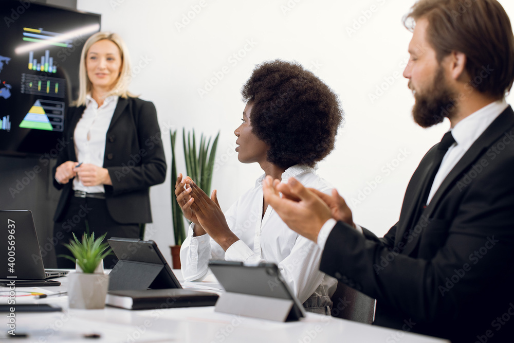 Close up of happy satisfied corporative workers, Caucasian male and African female business people, clapping hands after professional speech of her blond female boss. Focus on black lady Close up of happy satisfied corporative workers, Caucasian male and African female business people, clapping hands after professional speech of her blond female boss. Focus on black lady