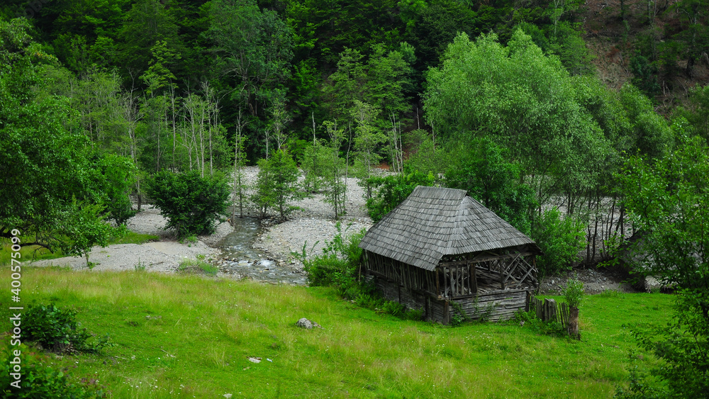 A rustic wooden cabin on a green alpine meadow. A mountain brook flows near it. Countryside panorama from Carpathian Mountains, Romania - Eastern Europe.