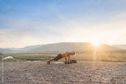 Athletic young man making push-ups outdoors on the mountain hill at sunset.