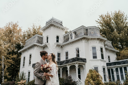 Young couple kissing in front of historic victorian era home on their wedding day photo
