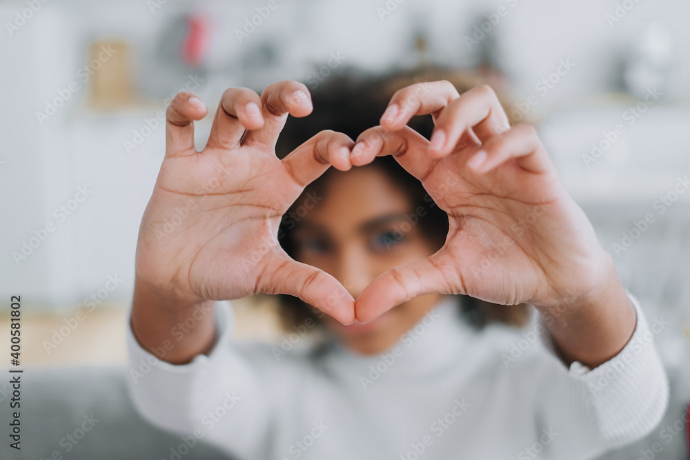 Cheerful dark skinned lady with kinky hair holds fingers in heart shape and showing to camera smiling widely close view Cheerful dark skinned lady with kinky hair holds fingers in heart shape and showing to camera smiling widely close view
