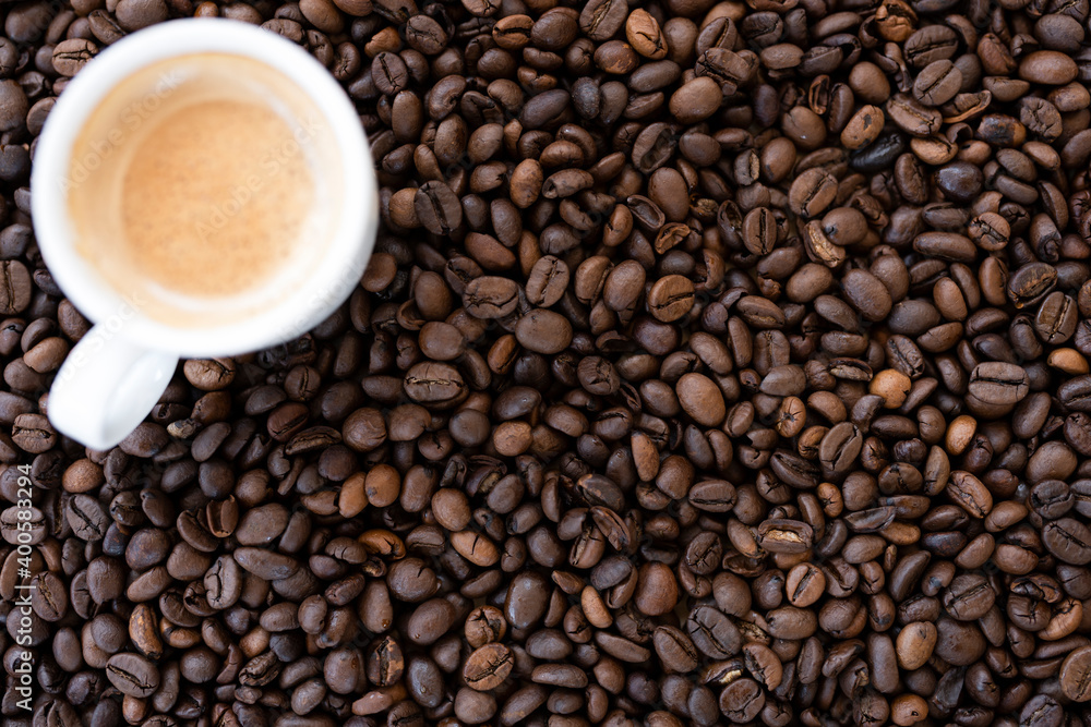 Flat lay with copy space, (selective focus) A defocused white espresso cup with some creamy coffee is placed on some roasted coffee beans. Flat lay with copy space, (selective focus) A defocused white espresso cup with some creamy coffee is placed on some roasted coffee beans.
