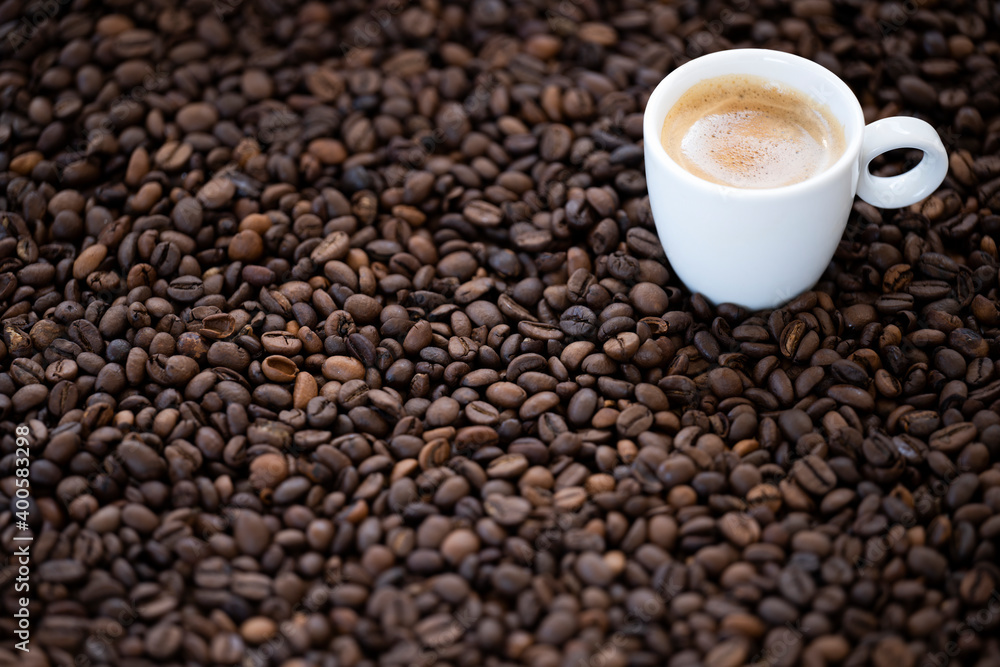 Flat lay with copy space, (selective focus) A white espresso cup with some creamy coffee is placed on some roasted coffee beans. Flat lay with copy space, (selective focus) A white espresso cup with some creamy coffee is placed on some roasted coffee beans.
