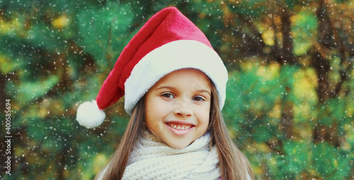 Christmas portrait of happy smiling little girl child in santa red hat outdoors