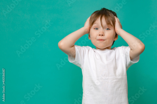 stylish child of four or five years old and holding his hands to his face he is surprised on a green background. Emotional boy posing for the camera