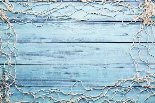 Frame made of fish net on color wooden background