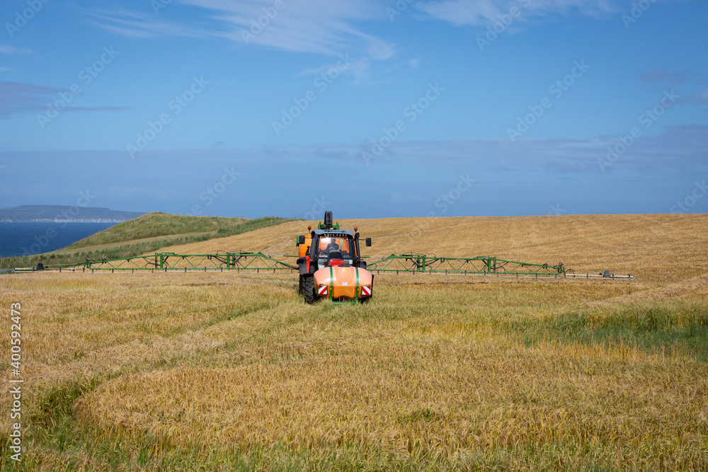 Naklejka premium crop sprayer treats field of barley on north coast northern ireland