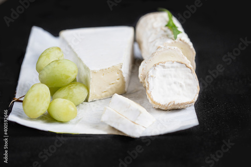 White goat cheese wih green grape on a  black background. Fresh goat cheese with copy space, cut in pieces